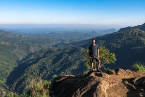 Steffen steht auf einem Berg mit Aussicht auf eine weite und dunstverhangene Berglandschaft.