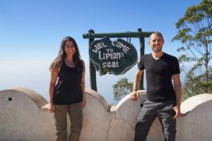 Farina und Steffen stehen vor einer weißen Mauer an einem Schild am Aussichtspunkt des Lipton's Seat