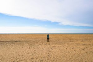 Steffen steht mit Cowboyhut auf einer weiten und menschenleeren Sandfläche am Meer