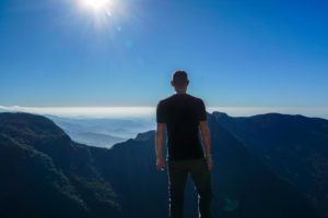Steffen schaut über eine dunkle Berglandschaft, die Sonne steht hell am kräftig blauen Himmel, während das Tal im Nebel verschwimmt.