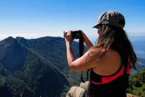 Farina sitzt auf einer Felsklippe mit Blick auf Berge und hält einen Fotoapparat in der Hand