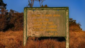 Ein grünes Willkommenschild steht in einer Buschlandschaft im Horton Plains Nationalpark.