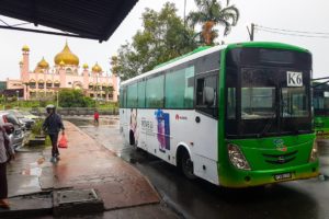 Ein grünweißer Bus mit der Nummer K6 hält vor einer rosa und goldenen Moschee in Kuching auf Borneo.