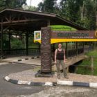 Farina steht unter dem Eingangsschild des Semenggho Wildlife Centre vor einem großen Unterstand an einem Weg im Park.