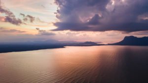 Ein weites Meer ist in abendlichen Rosa- und Blautönen gefärbt vor dem Hintergrund der vorbeiziehenden Wolken.