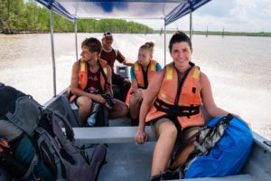 Farina sitzt mit anderen Menschen in einem kleinen Boot auf einem Fluss, alle haben orange Rettungswesten an.