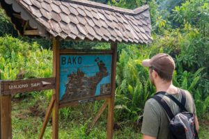 Steffen steht vor einem blauen Hinweisschild im Naturschutzgebiet, das die Wanderwege ausschildert.