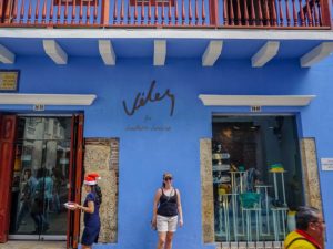Farina steht vor einer blauen Hauswand mit Geschäft.