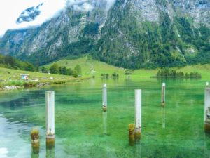 Pflöcke ragen aus dem flachen Wasser am Ufer des Königssees.